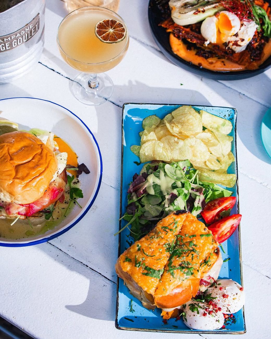 Open salmon sandwiches and a burger with salad and crisps on a blue plate