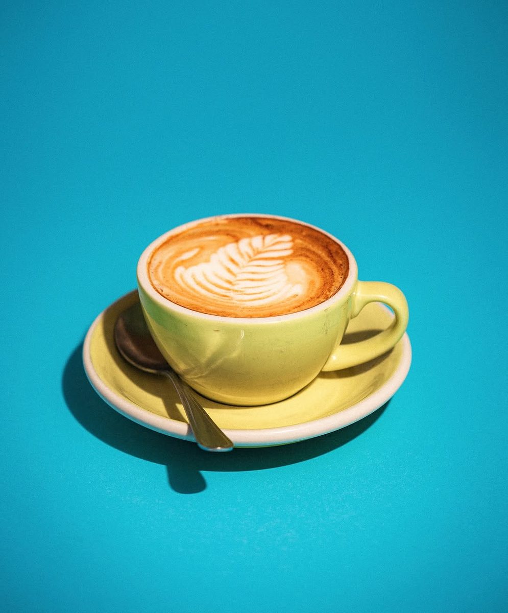 Cappuccino with leaf latte art in a yellow cup on a turquoise background