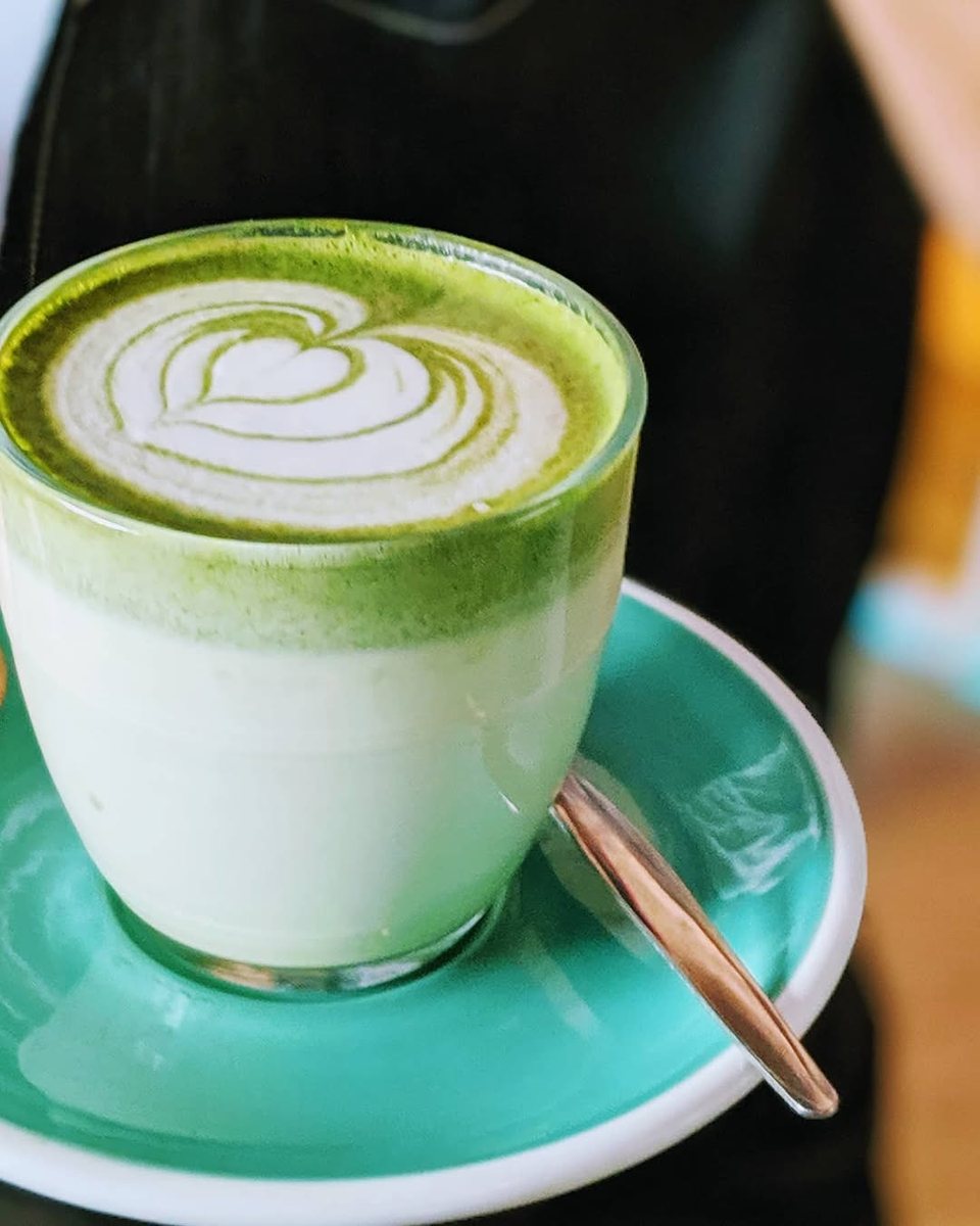 A matcha latte with leaf art in a glass on a turquoise saucer