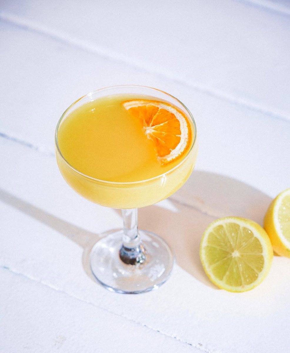 A mimosa in a coupe glass with a dried orange slice and fresh lemons