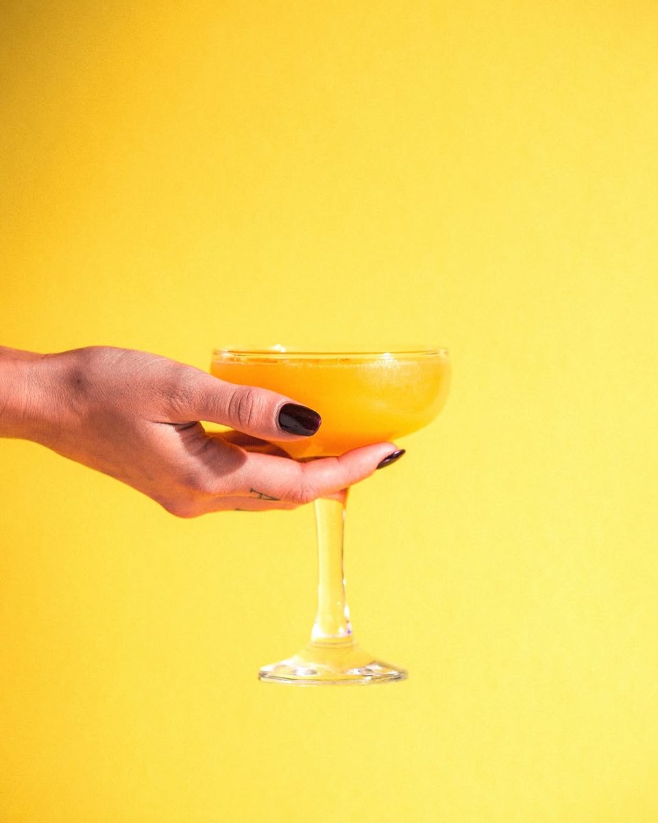 A hand holding a mimosa coupe against a bright yellow background