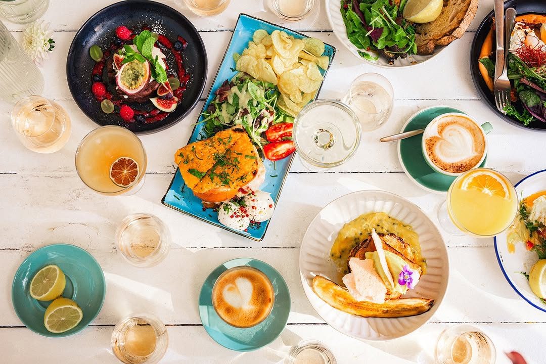 Brunch plates, coffees and glasses spread across a white wooden table