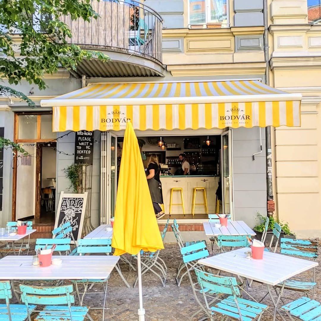 The striped awning over turquoise terrace chairs and white tables on the street