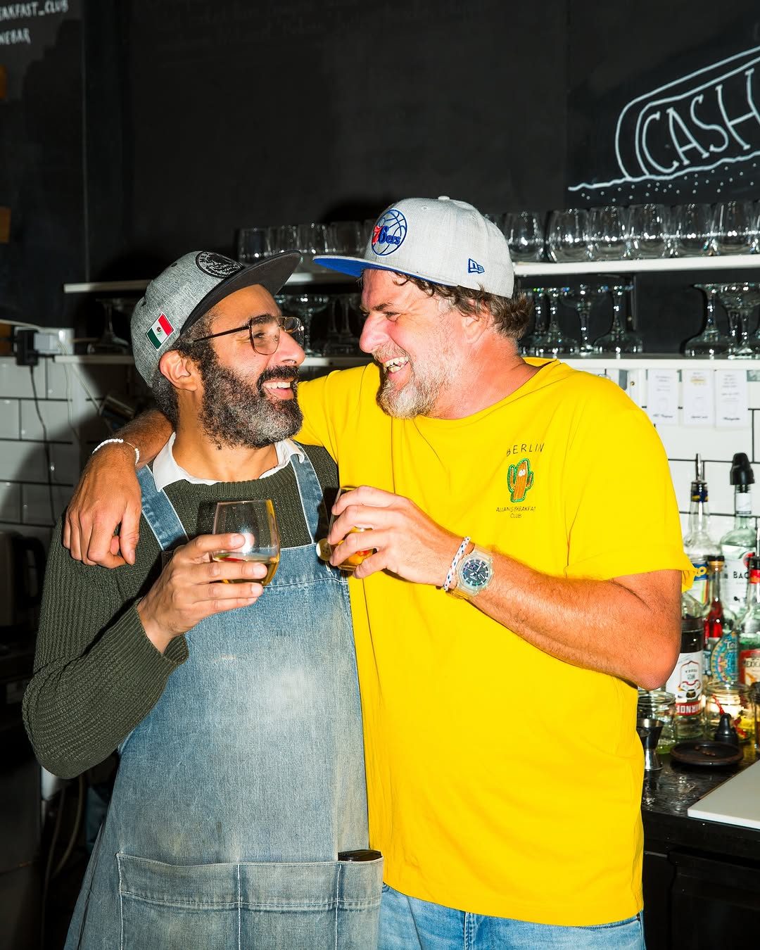 Two of the team laughing together behind the bar with drinks in hand