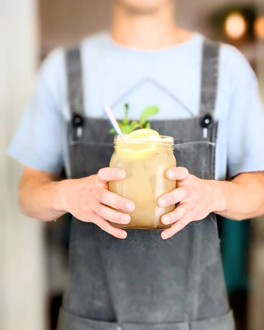 A member of the team in an apron carrying a tall iced drink to a table